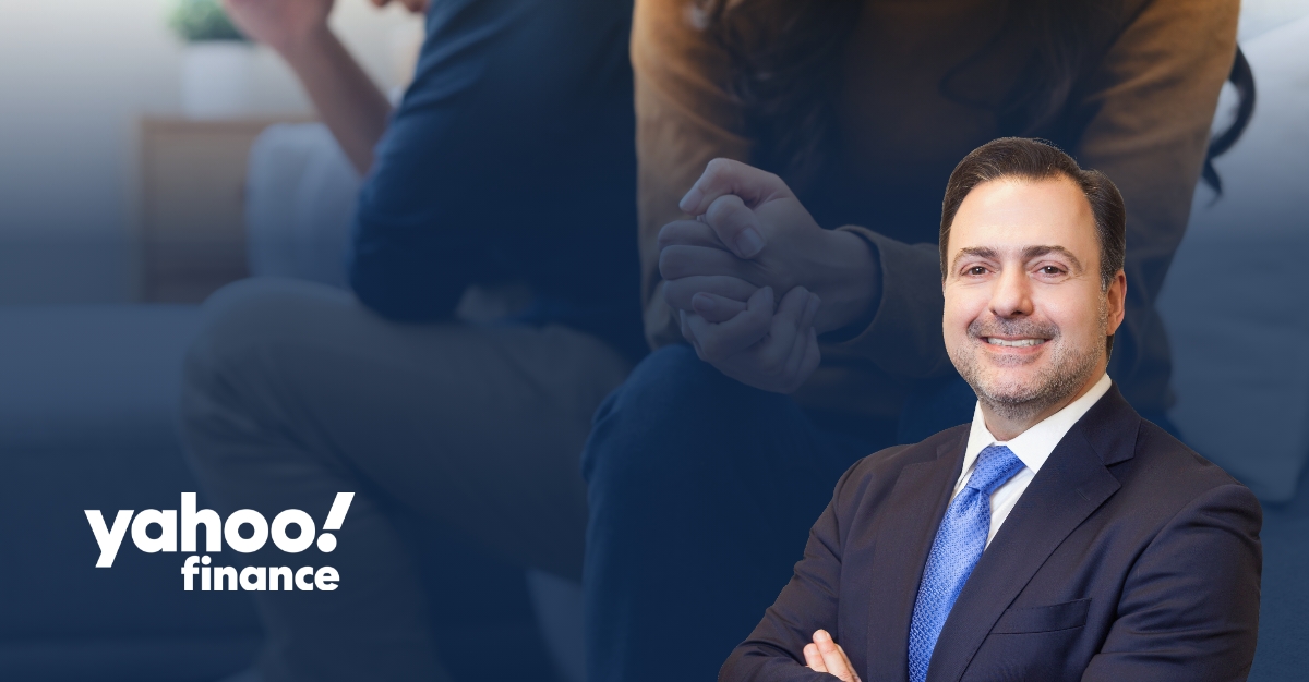Asher Rubinstein in a dark suit and blue tie, smiling with his arms crossed. The background shows a blurred image of a couple sitting apart with clasped hands, suggesting financial or relationship challenges. The Yahoo Finance logo appears in the lower left corner. The image conveys themes of financial planning, asset protection, and legal guidance during divorce or other major life transitions.