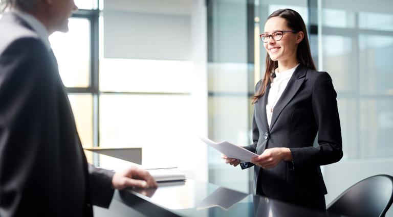 man talking with a smiling woman standing up at desk