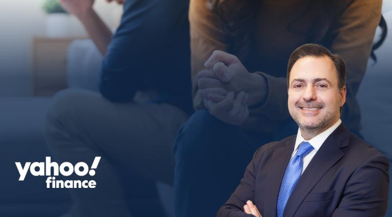Asher Rubinstein in a dark suit and blue tie, smiling with his arms crossed. The background shows a blurred image of a couple sitting apart with clasped hands, suggesting financial or relationship challenges. The Yahoo Finance logo appears in the lower left corner. The image conveys themes of financial planning, asset protection, and legal guidance during divorce or other major life transitions.
